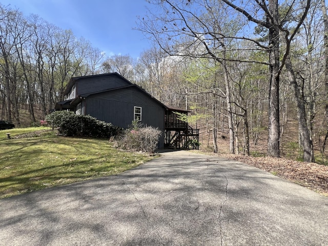view of side of home with a yard, driveway, and a view of trees