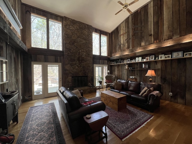 living room featuring wooden walls, high vaulted ceiling, a fireplace, and a ceiling fan