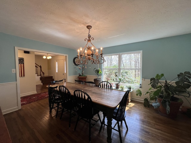 dining space featuring a textured ceiling, stairway, hardwood / wood-style floors, baseboards, and a notable chandelier