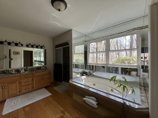 full bath featuring a sink, double vanity, a whirlpool tub, a shower stall, and hardwood / wood-style floors