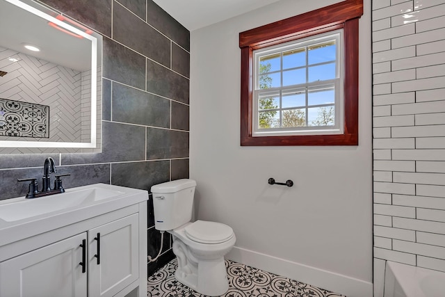 bathroom with vanity, toilet, tile walls, tile patterned floors, and baseboards