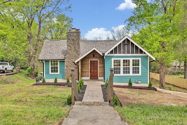 view of front of house featuring a front yard, a chimney, fence, and roof with shingles