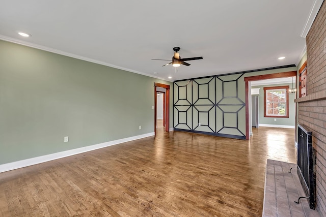 unfurnished living room with crown molding, a ceiling fan, wood finished floors, a brick fireplace, and baseboards