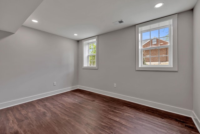 empty room featuring a wealth of natural light, dark wood-type flooring, visible vents, and baseboards