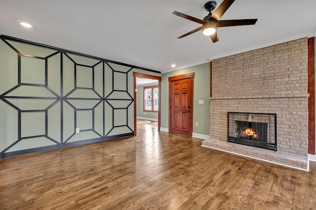 unfurnished living room featuring baseboards, ornamental molding, a ceiling fan, a fireplace, and wood finished floors