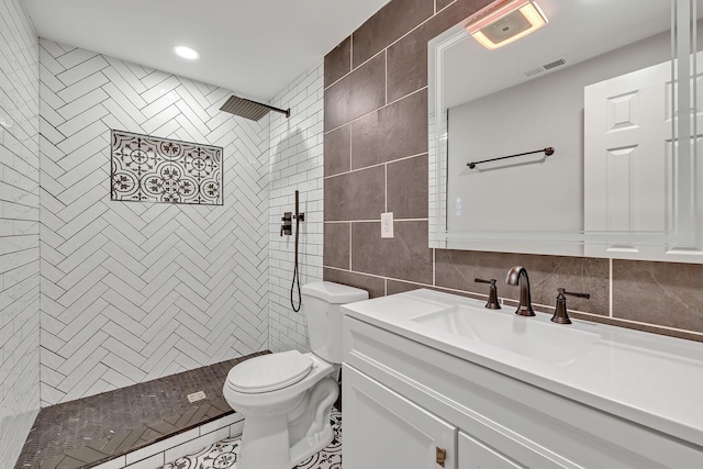 bathroom featuring tiled shower, vanity, visible vents, toilet, and tile walls