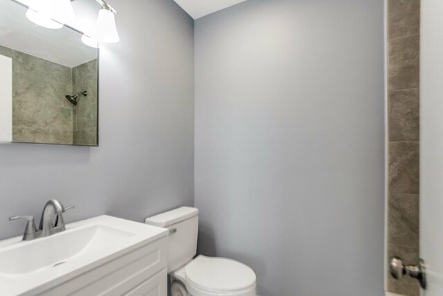 bathroom featuring toilet, vanity, and a tile shower