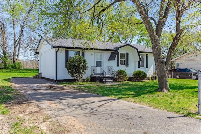 single story home with aphalt driveway, a shingled roof, and a front lawn