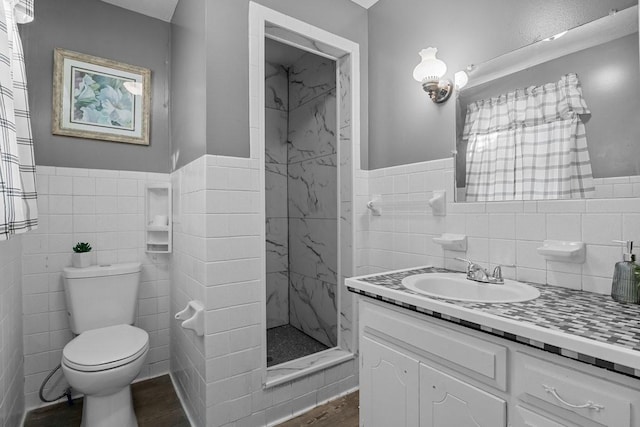 bathroom featuring tile walls, a shower stall, wainscoting, wood finished floors, and vanity