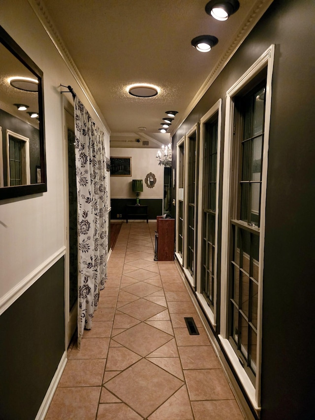 hall with light tile patterned floors, visible vents, a textured ceiling, and crown molding