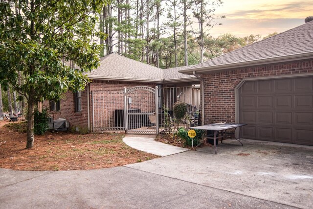 exterior space featuring roof with shingles, brick siding, a gate, an attached garage, and driveway