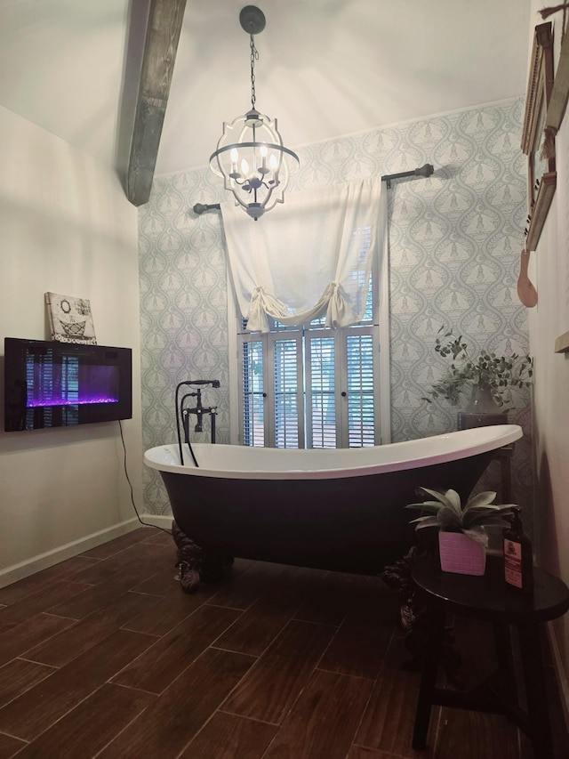 bathroom featuring a notable chandelier, baseboards, wallpapered walls, a freestanding bath, and wood finished floors