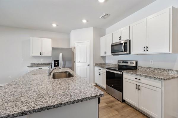 kitchen with light stone counters, white cabinets, visible vents, stainless steel appliances, and a sink
