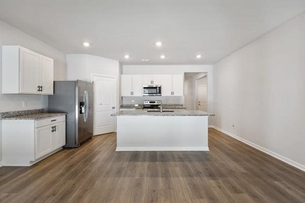 kitchen with white cabinetry, stainless steel appliances, a center island with sink, baseboards, and dark wood-style floors