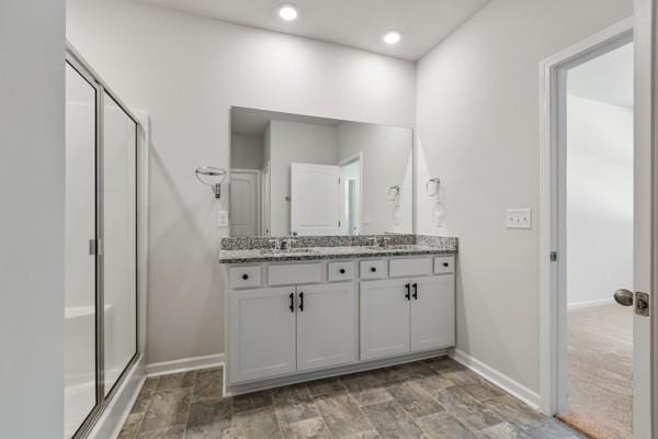 full bathroom featuring baseboards, a shower stall, and double vanity