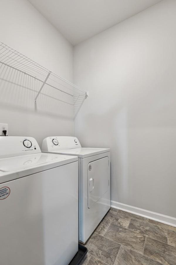 clothes washing area with laundry area, stone finish floor, baseboards, and washer and clothes dryer