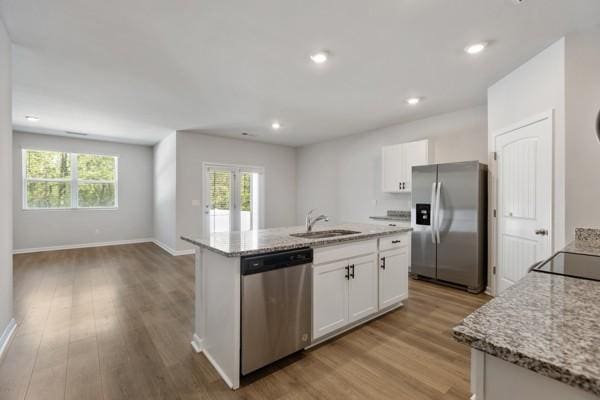 kitchen featuring an island with sink, white cabinets, appliances with stainless steel finishes, light wood finished floors, and a sink