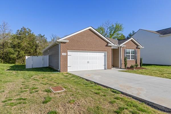 view of front facade with concrete driveway, a front lawn, an attached garage, brick siding, and fence