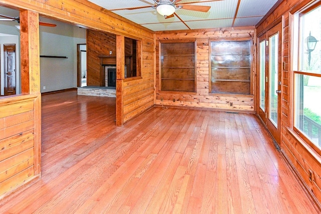 empty room featuring wooden walls, wood-type flooring, a ceiling fan, and a glass covered fireplace