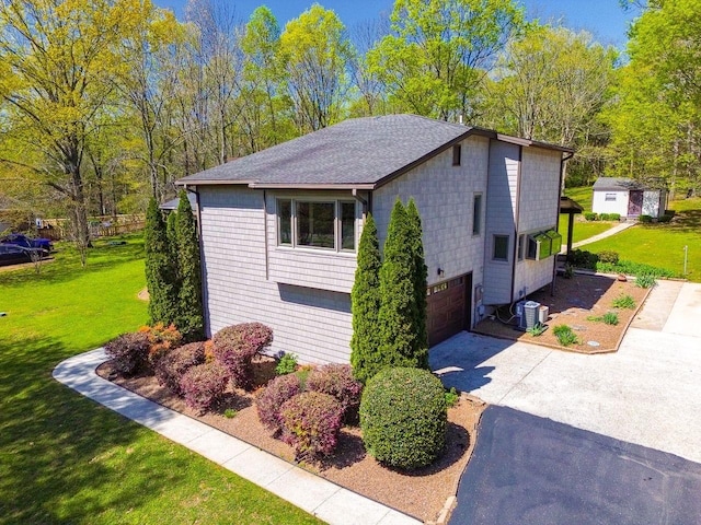 view of side of property with driveway, central AC unit, a garage, a yard, and a shingled roof