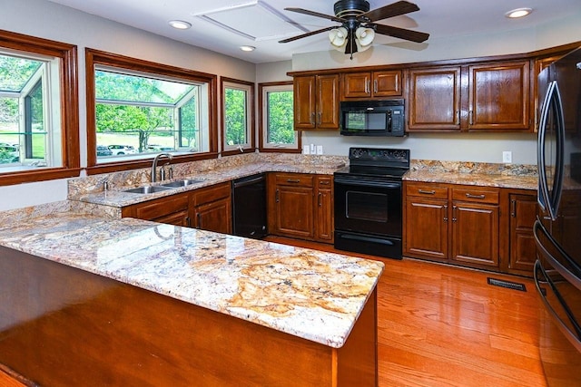 kitchen with ceiling fan, light stone countertops, a peninsula, black appliances, and a sink