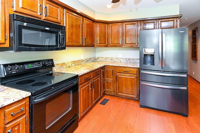 kitchen featuring light wood-type flooring, a ceiling fan, black appliances, light stone counters, and brown cabinets