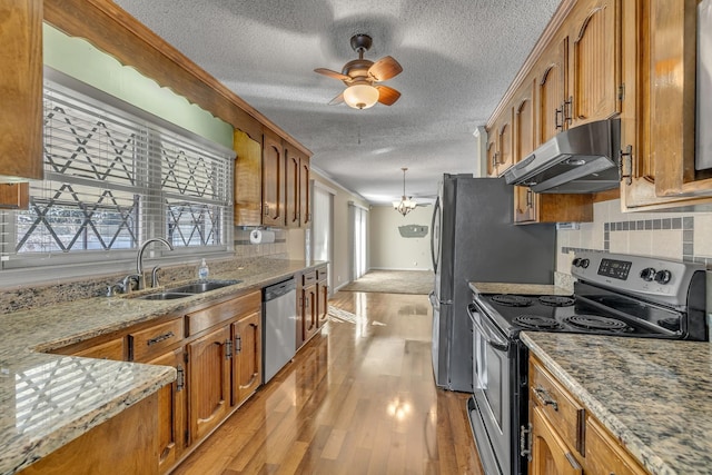 kitchen featuring light wood-style flooring, brown cabinetry, under cabinet range hood, a sink, and stainless steel appliances