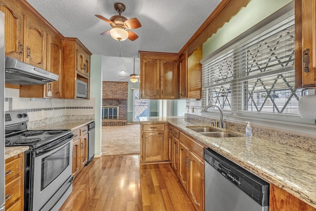 kitchen with a ceiling fan, appliances with stainless steel finishes, under cabinet range hood, a sink, and brown cabinets
