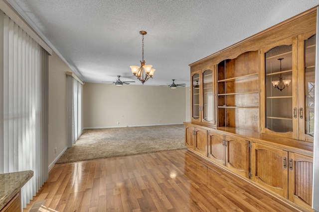 unfurnished dining area with light wood-style flooring, a textured ceiling, ceiling fan with notable chandelier, and baseboards