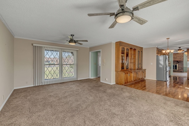 unfurnished living room featuring a textured ceiling, ceiling fan with notable chandelier, ornamental molding, and carpet floors