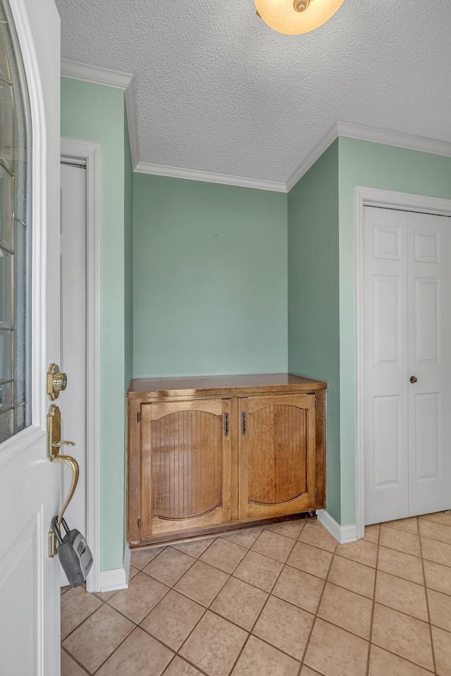 interior space featuring light tile patterned floors, baseboards, ornamental molding, and a textured ceiling