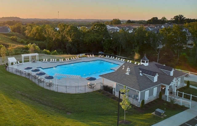 pool at dusk with a pergola, a yard, a community pool, fence, and a patio