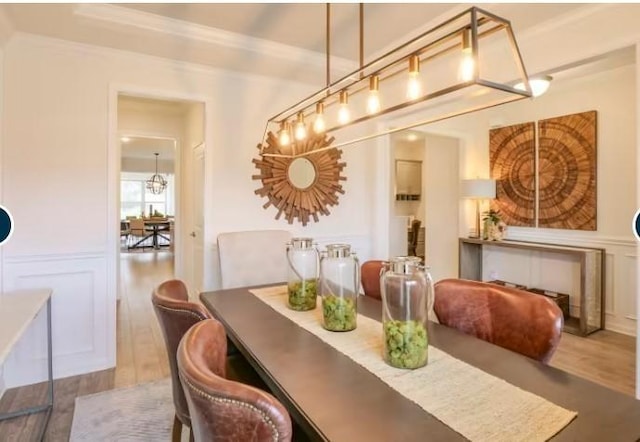 dining space featuring a chandelier, wood finished floors, a wainscoted wall, and a decorative wall