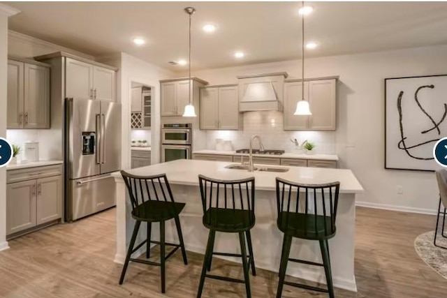 kitchen featuring light wood-style floors, an island with sink, tasteful backsplash, appliances with stainless steel finishes, and light countertops