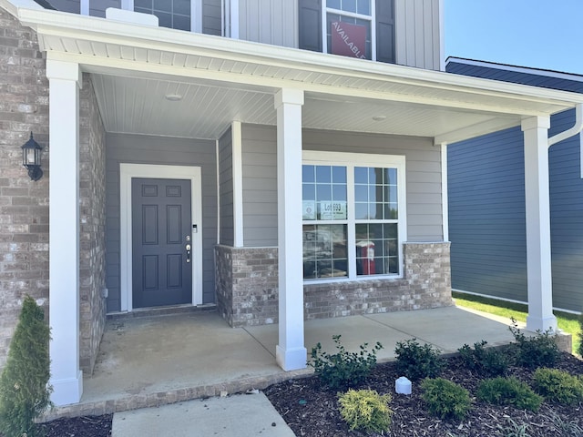 doorway to property with brick siding, board and batten siding, and covered porch