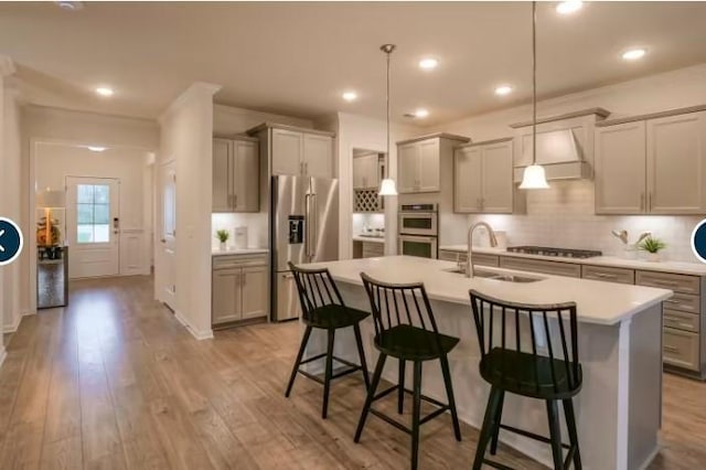 kitchen with light countertops, a center island with sink, a breakfast bar area, stainless steel appliances, and a sink