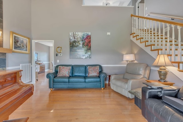 living room featuring a high ceiling, visible vents, stairway, and light wood-style floors
