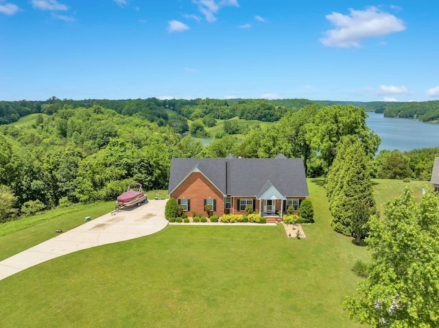 view of front of house with concrete driveway, a water view, a front yard, and a forest view