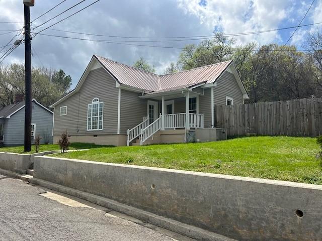 view of front of property featuring a front yard, metal roof, fence, and covered porch