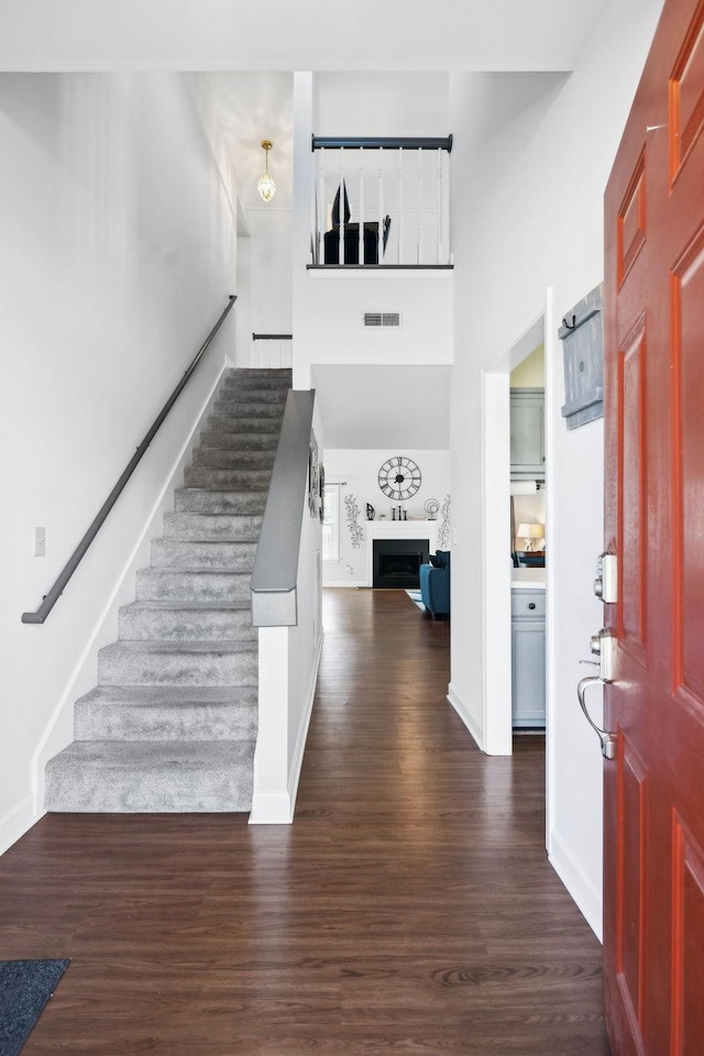 foyer entrance with visible vents, baseboards, a fireplace, stairway, and wood finished floors
