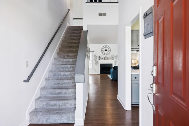 entryway with a fireplace, dark wood-style floors, visible vents, and stairs