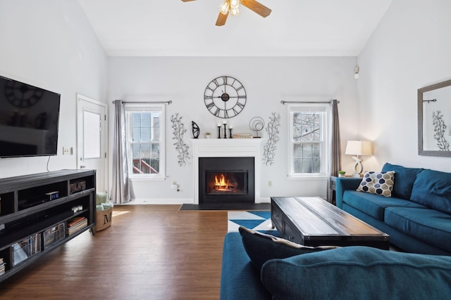 living area with a fireplace with flush hearth, wood finished floors, ceiling fan, and baseboards