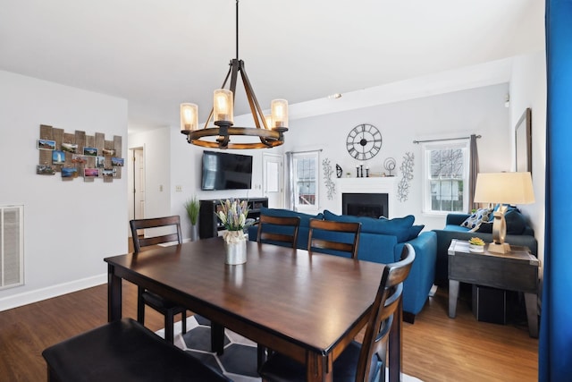 dining room with baseboards, an inviting chandelier, a fireplace, visible vents, and wood finished floors
