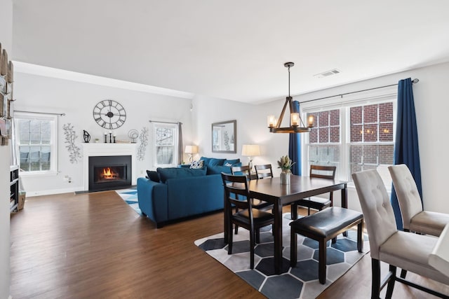 dining area with visible vents, baseboards, a notable chandelier, dark wood-style flooring, and a lit fireplace