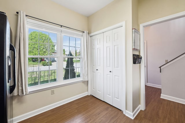 unfurnished bedroom with a closet, baseboards, black refrigerator with ice dispenser, and wood finished floors