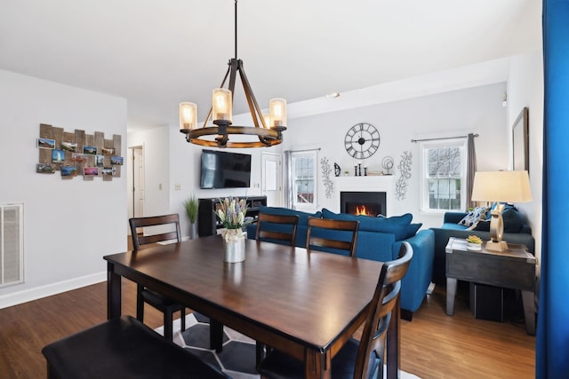 dining room featuring dark wood finished floors, a lit fireplace, visible vents, a chandelier, and baseboards