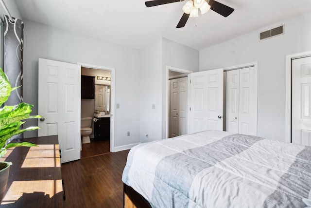 bedroom with dark wood-style flooring, baseboards, ensuite bath, visible vents, and multiple closets