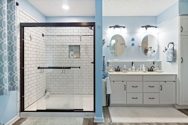 bathroom with double vanity, a stall shower, and wood finished floors