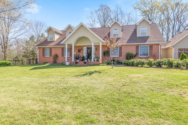 view of front of house with a shingled roof, brick siding, fence, and a front lawn