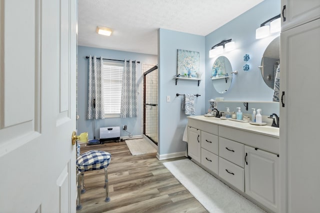 bathroom with a sink, a textured ceiling, double vanity, wood finished floors, and a stall shower